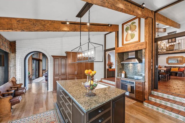32423 Womsi Rd, Pauma Valley, CA 92061 - kitchen with stainless steel oven, wall chimney range hood, arched walkways, a chandelier, and light stone countertops