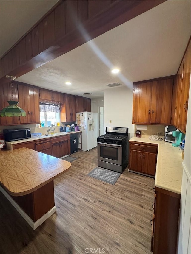 1004 Paloma St, Bakersfield, CA 93304 - kitchen featuring gas range, white refrigerator with ice dispenser, light countertops, brown cabinetry, and light wood-style flooring