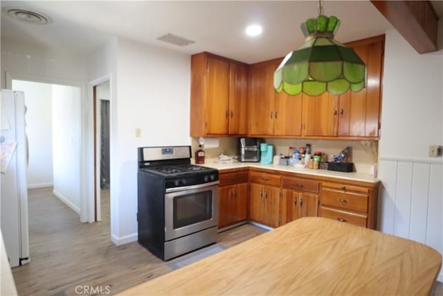 1004 Paloma St, Bakersfield, CA 93304 - kitchen with gas stove, freestanding refrigerator, light countertops, light wood finished floors, and brown cabinetry