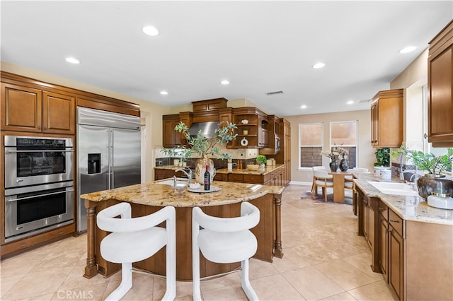 27684 Manor Hill Rd, Laguna Niguel, CA 92677 - kitchen featuring stainless steel appliances, a kitchen island with sink, light stone counters, open shelves, and a breakfast bar area