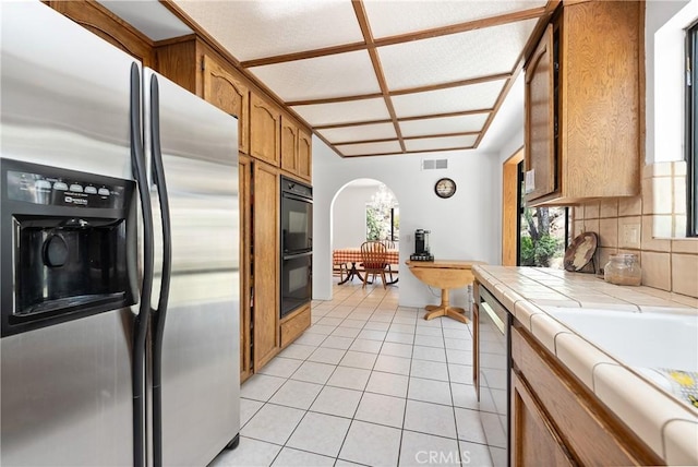 9349 Hartman Way, West Hills, CA 91304 - kitchen featuring stainless steel appliances, tile countertops, arched walkways, light tile patterned flooring, and decorative backsplash