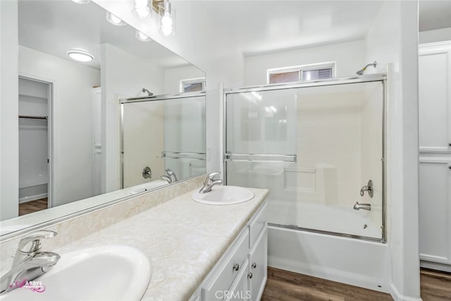 bathroom with double vanity, enclosed tub / shower combo, wood finished floors, and a walk in closet