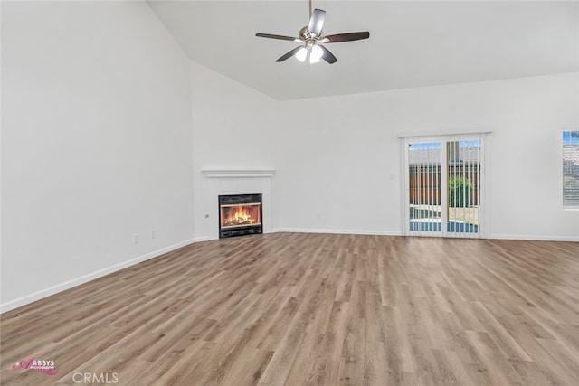 unfurnished living room featuring light wood finished floors, a ceiling fan, a glass covered fireplace, and high vaulted ceiling