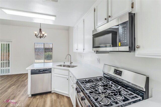 kitchen featuring appliances with stainless steel finishes, a peninsula, white cabinets, and a chandelier
