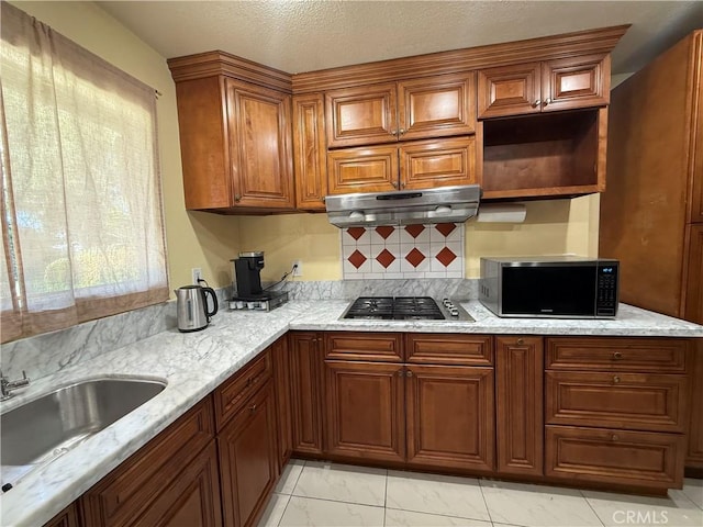 11057 Dudley Way, Stanton, CA 90680 - kitchen with under cabinet range hood, stainless steel gas cooktop, brown cabinetry, light stone countertops, and a textured ceiling