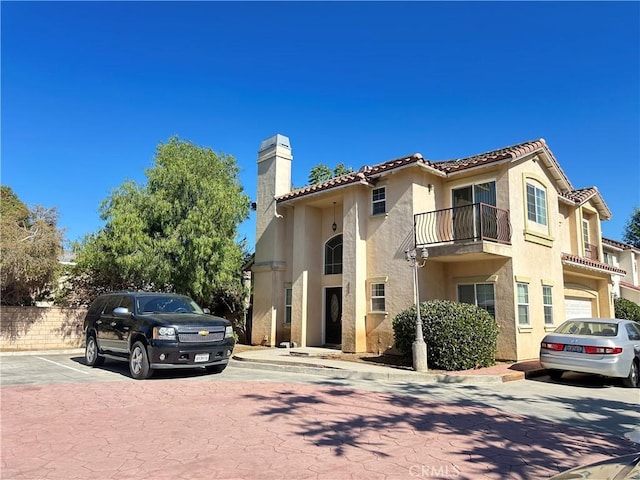 606 W Grand Ave, Pomona, CA 91766 - view of front of property featuring a chimney, a balcony, stucco siding, a tiled roof, and uncovered parking