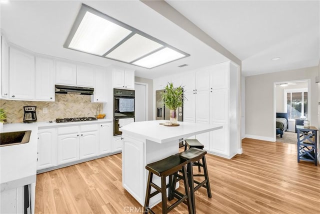 12312 Marmont Pl, Moreno Valley, CA 92557 - kitchen with under cabinet range hood, light countertops, white cabinetry, a breakfast bar, and recessed lighting