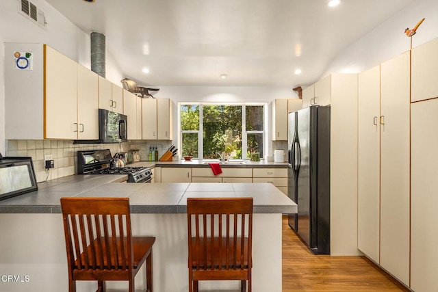 840 Fairview Rd, Ojai, CA 93023 - kitchen with black appliances, a peninsula, recessed lighting, cream cabinetry, and light wood-style floors