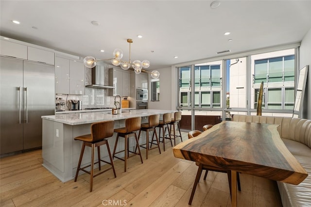 3306 Via Oporto, Newport Beach, CA 92663 - kitchen featuring stainless steel appliances, modern cabinets, light wood-style flooring, wall chimney range hood, and backsplash