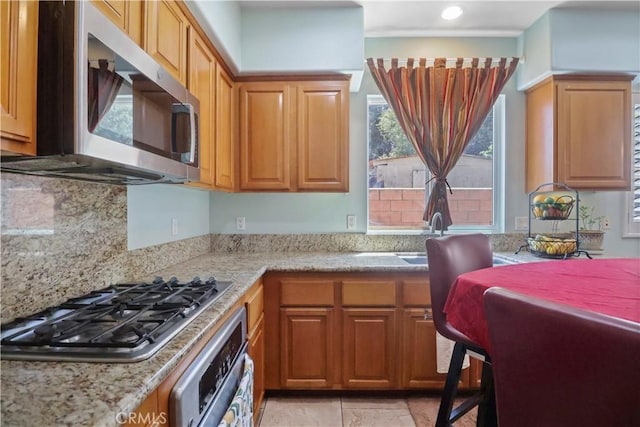 9044 Sylmar Ave, Panorama City, CA 91402 - kitchen with stainless steel appliances, decorative backsplash, brown cabinetry, and light stone countertops