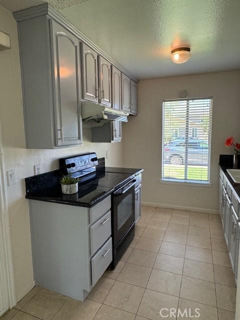 1353 E Fairgrove Ave Unit 293, West Covina, CA 91792 - kitchen with black range with electric cooktop, under cabinet range hood, dark countertops, light tile patterned floors, and a textured ceiling