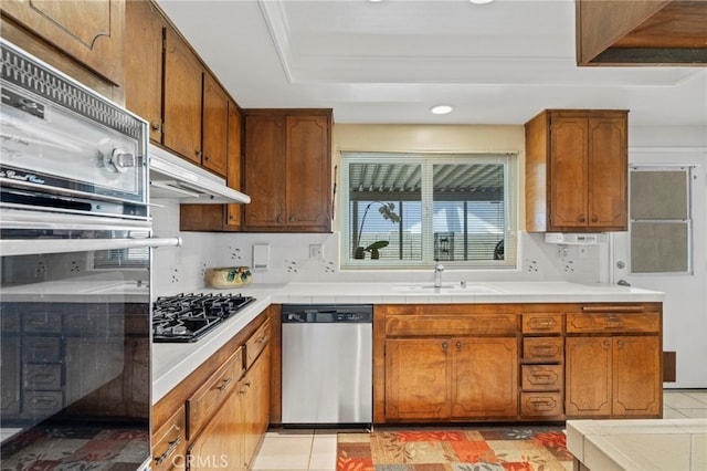 3186 N Hartman St, Orange, CA 92865 - kitchen with appliances with stainless steel finishes, under cabinet range hood, brown cabinets, recessed lighting, and tile counters