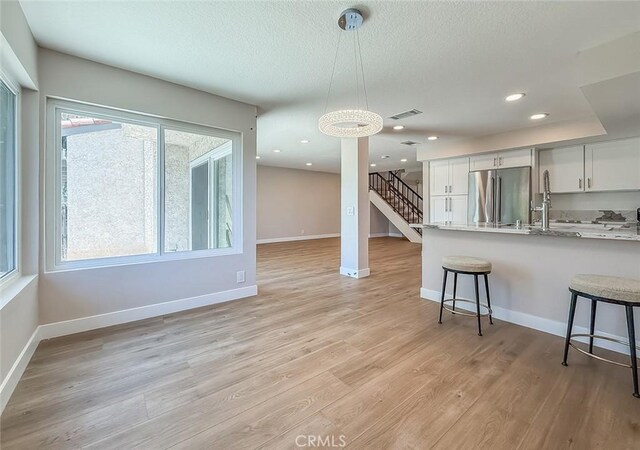19237 Index St Unit 5, Porter Ranch, CA 91326 - kitchen with stainless steel fridge, a kitchen bar, white cabinets, hanging light fixtures, and light wood-type flooring