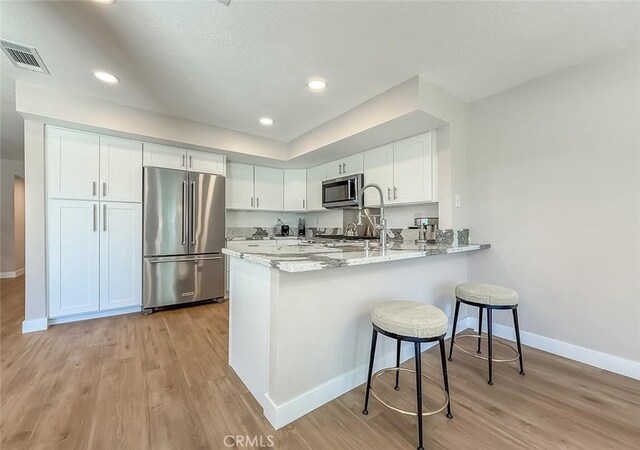 19237 Index St Unit 5, Porter Ranch, CA 91326 - kitchen with stainless steel appliances, a peninsula, light wood finished floors, white cabinets, and a kitchen breakfast bar