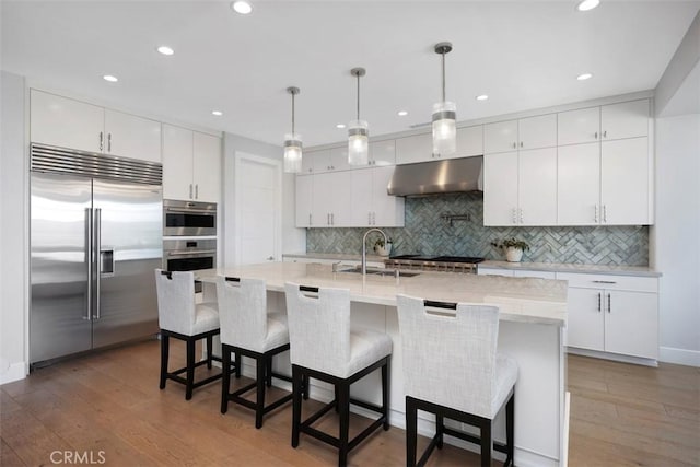 27705 Homestead Rd, Laguna Niguel, CA 92677 - kitchen featuring stainless steel appliances, under cabinet range hood, tasteful backsplash, wood finished floors, and white cabinets