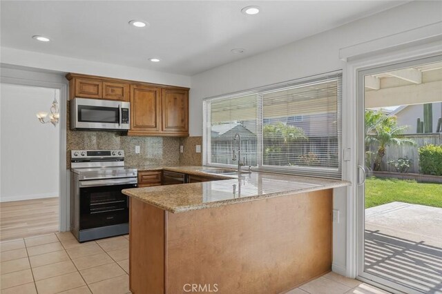 14652 Devonshire Ave, Tustin, CA 92780 - kitchen featuring appliances with stainless steel finishes, light stone counters, a peninsula, brown cabinetry, and light tile patterned floors