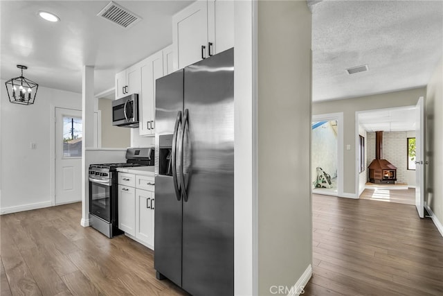 835 E 222nd St, Carson, CA 90745 - kitchen with stainless steel appliances, a wood stove, white cabinets, wood finished floors, and light countertops