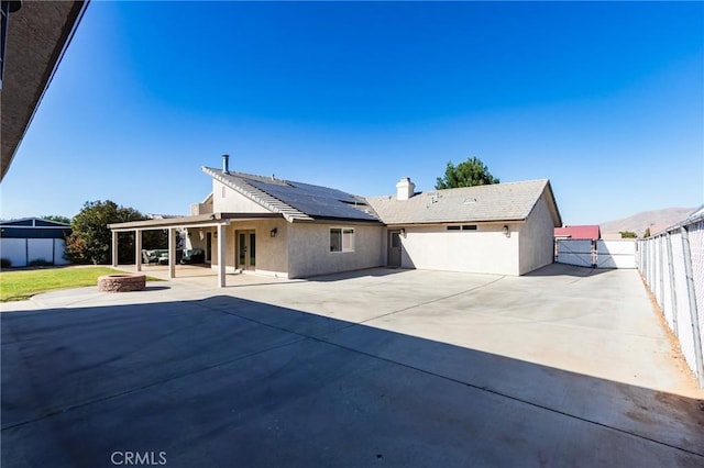 7434 Paisley Ave, Hesperia, CA 92345 - rear view of house with a fenced backyard, roof mounted solar panels, a patio, stucco siding, and a chimney