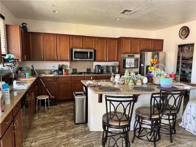 1465 Ardith Ct, Beaumont, CA 92223 - kitchen with stainless steel appliances, a breakfast bar, an island with sink, and light stone counters