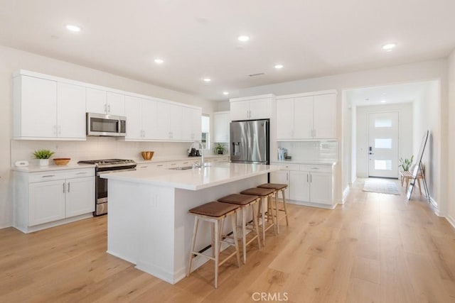4835 S Cora Way, Ontario, CA 91762 - kitchen featuring appliances with stainless steel finishes, decorative backsplash, a kitchen breakfast bar, light wood-style flooring, and a center island with sink