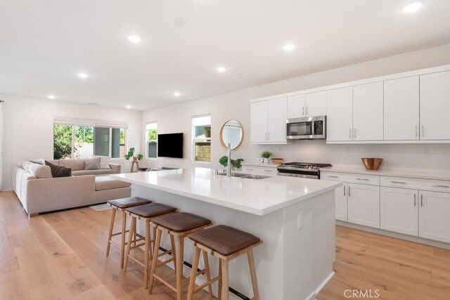 4835 S Cora Way, Ontario, CA 91762 - kitchen featuring appliances with stainless steel finishes, a kitchen bar, light wood-style flooring, backsplash, and white cabinetry