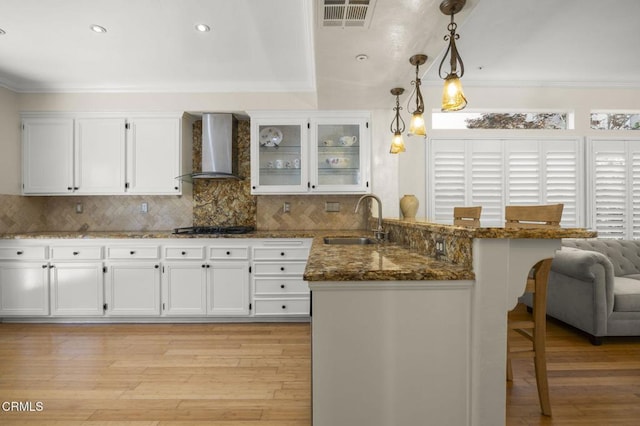 7748 Paso Robles St, Ventura, CA 93004 - kitchen with wall chimney exhaust hood, a peninsula, a kitchen breakfast bar, white cabinets, and light wood-style flooring