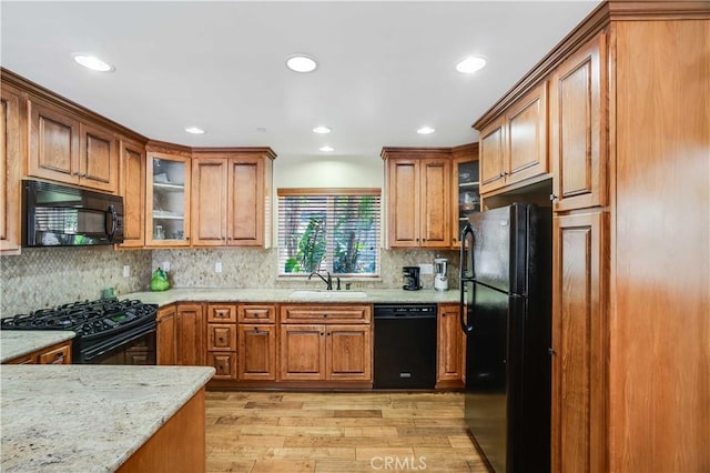 21460 Arapahoe Trl, Chatsworth, CA 91311 - kitchen with black appliances, brown cabinetry, light wood-style flooring, light stone counters, and glass insert cabinets
