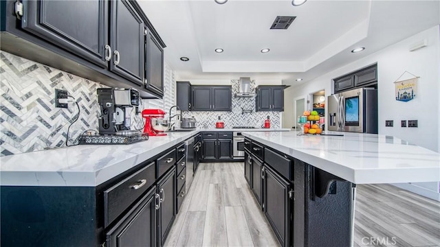 18223 Shannon Ridge Pl, Canyon Country, CA 91387 - kitchen with appliances with stainless steel finishes, dark cabinetry, wall chimney range hood, light wood finished floors, and recessed lighting