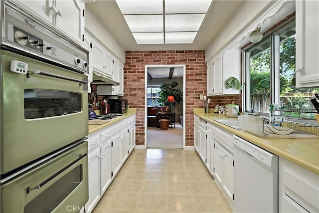 2997 June Ct, Merced, CA 95348 - kitchen with white dishwasher, white cabinets, light countertops, light tile patterned flooring, and brick wall