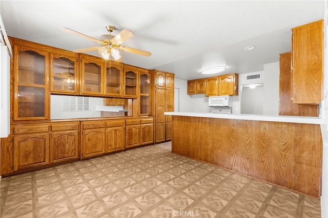 16257 Avalon Ave, Victorville, CA 92395 - kitchen with white microwave, brown cabinetry, light floors, a peninsula, and a ceiling fan