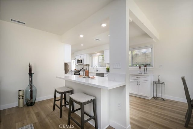 1610 Wandering Dr, Monterey Park, CA 91754 - kitchen featuring a breakfast bar area, white cabinets, wood finished floors, appliances with stainless steel finishes, and recessed lighting
