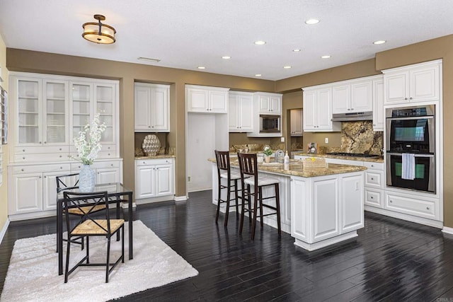 27002 Red Maple St, Murrieta, CA 92562 - kitchen featuring appliances with stainless steel finishes, under cabinet range hood, white cabinetry, backsplash, and a breakfast bar area