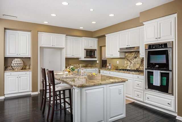 27002 Red Maple St, Murrieta, CA 92562 - kitchen featuring appliances with stainless steel finishes, under cabinet range hood, dark wood-style floors, white cabinets, and recessed lighting