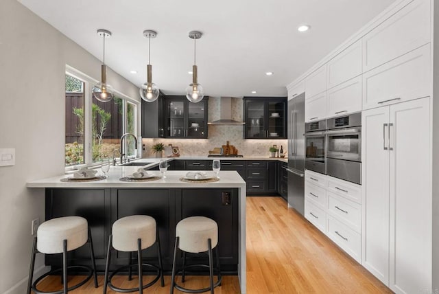 3903 Cadden Way, San Diego, CA 92117 - kitchen featuring wall chimney range hood, glass insert cabinets, a peninsula, light countertops, and a kitchen breakfast bar