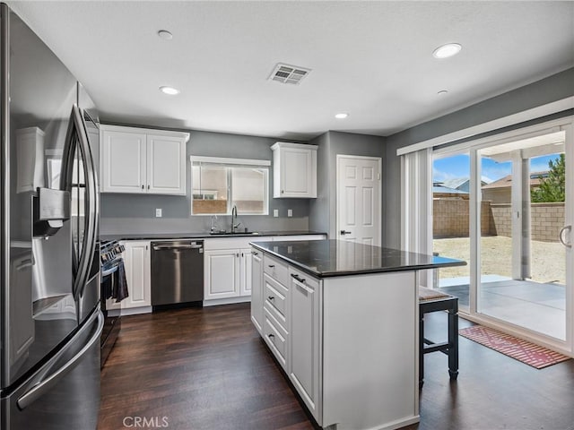 11760 Espola Pl, Victorville, CA 92392 - kitchen with stainless steel appliances, dark countertops, white cabinetry, a breakfast bar, and recessed lighting