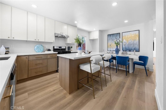 1851 S San Antonio Ave, Pomona, CA 91766 - kitchen with stainless steel gas range, under cabinet range hood, light wood-style flooring, a breakfast bar, and white cabinets