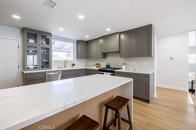 7830 Fairchild Ave, Winnetka, CA 91306 - kitchen with stainless steel dishwasher, gray cabinets, range with gas stovetop, light stone countertops, and backsplash