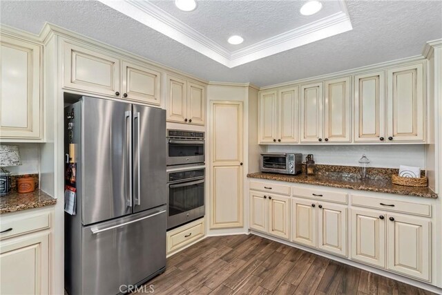 9292 Garden St, Rancho Cucamonga, CA 91701 - kitchen featuring appliances with stainless steel finishes, cream cabinets, a textured ceiling, dark wood-style floors, and dark stone counters