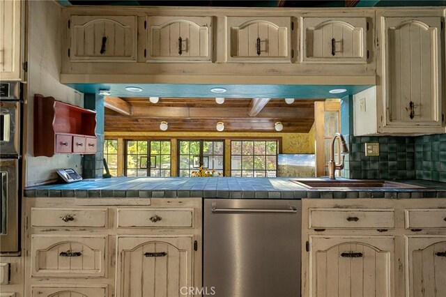 969 Oak Dr, Crestline, CA 92325 - kitchen featuring stainless steel appliances, tile counters, cream cabinets, tasteful backsplash, and beamed ceiling