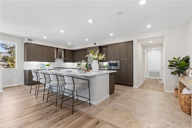 107 Bowery, Irvine, CA 92612 - kitchen with stainless steel microwave, wall chimney range hood, dark brown cabinets, light countertops, and a large island with sink