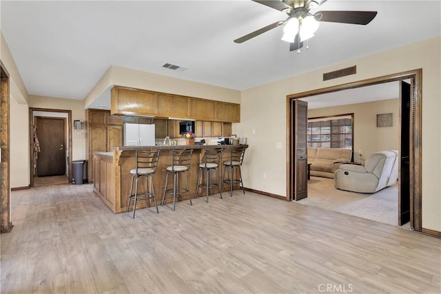 7505 Jenkins Ave, Hesperia, CA 92345 - kitchen featuring freestanding refrigerator, brown cabinets, a breakfast bar area, a peninsula, and light wood finished floors