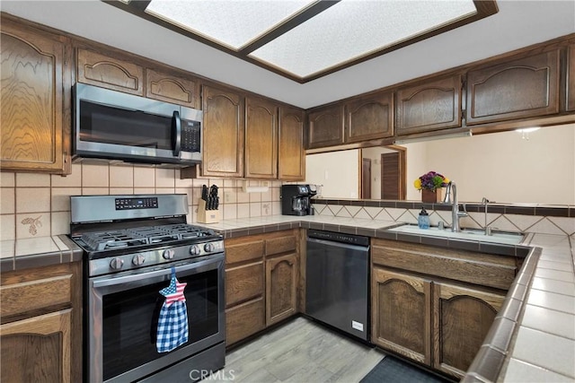 7505 Jenkins Ave, Hesperia, CA 92345 - kitchen featuring stainless steel appliances, tile counters, light wood-style flooring, and decorative backsplash