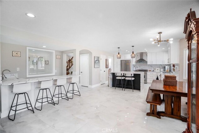 2741 Olympic View Dr, Chino Hills, CA 91709 - kitchen featuring a breakfast bar, wall chimney range hood, white cabinets, decorative backsplash, and a chandelier