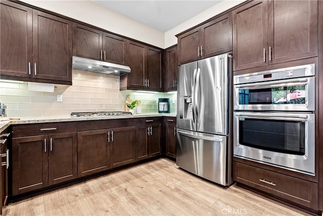 138 Listo St, Rancho Mission Viejo, CA 92694 - kitchen featuring appliances with stainless steel finishes, under cabinet range hood, dark brown cabinetry, backsplash, and light wood-style flooring