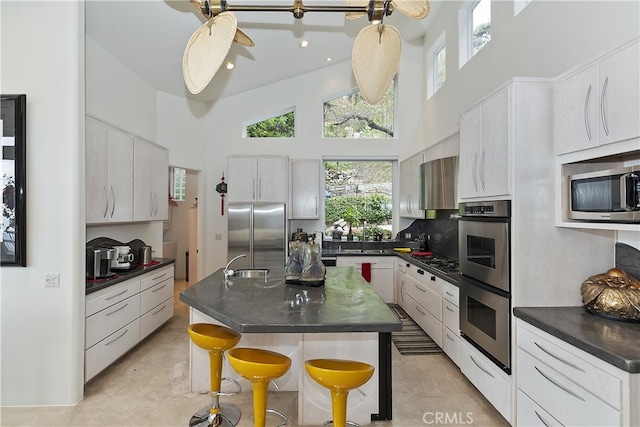 28527 Willow Rd, Lake Arrowhead, CA 92385 - kitchen featuring appliances with stainless steel finishes, a towering ceiling, dark countertops, healthy amount of natural light, and white cabinets