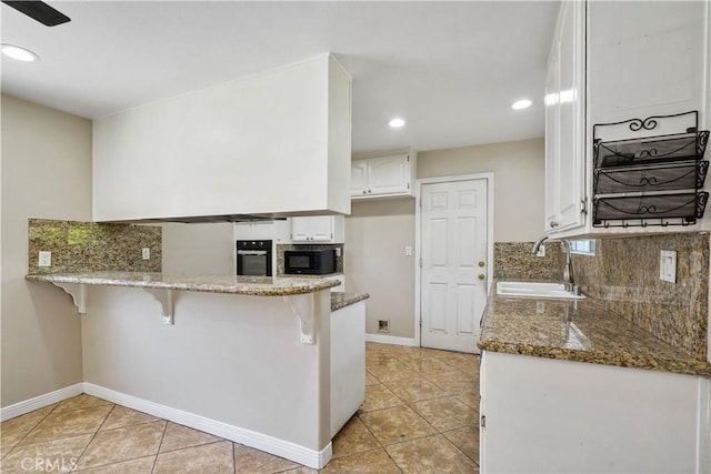 10265 Lev Ave, Arleta, CA 91331 - kitchen with black appliances, light tile patterned floors, dark stone countertops, a kitchen bar, and white cabinets