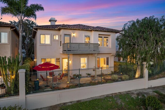 7243 Surfbird Cir, Carlsbad, CA 92011 - back of house at dusk with a balcony, a fenced backyard, a chimney, a tile roof, and stucco siding