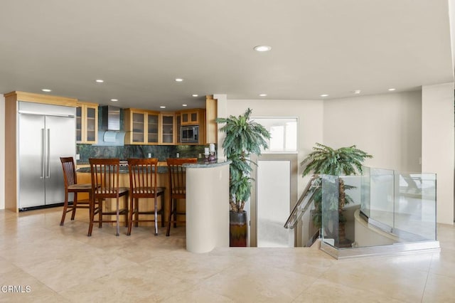 3629 Ocean Dr, Oxnard, CA 93035 - kitchen with built in appliances, recessed lighting, decorative backsplash, wall chimney range hood, and glass insert cabinets