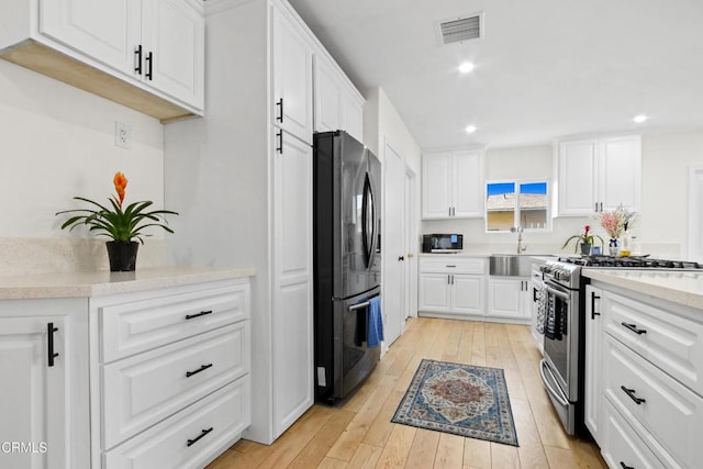 2165 W 115th St, Hawthorne, CA 90250 - kitchen featuring freestanding refrigerator, stainless steel gas range oven, white cabinets, light wood-type flooring, and recessed lighting