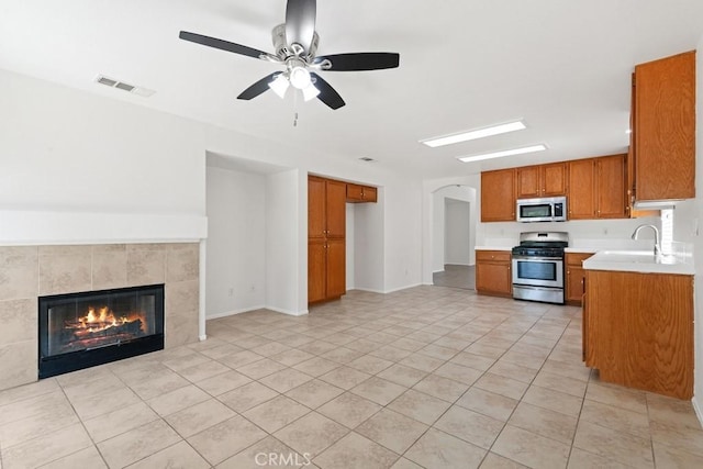5185 Konic Ct, Riverside, CA 92509 - kitchen featuring appliances with stainless steel finishes, brown cabinetry, light countertops, ceiling fan, and a tiled fireplace